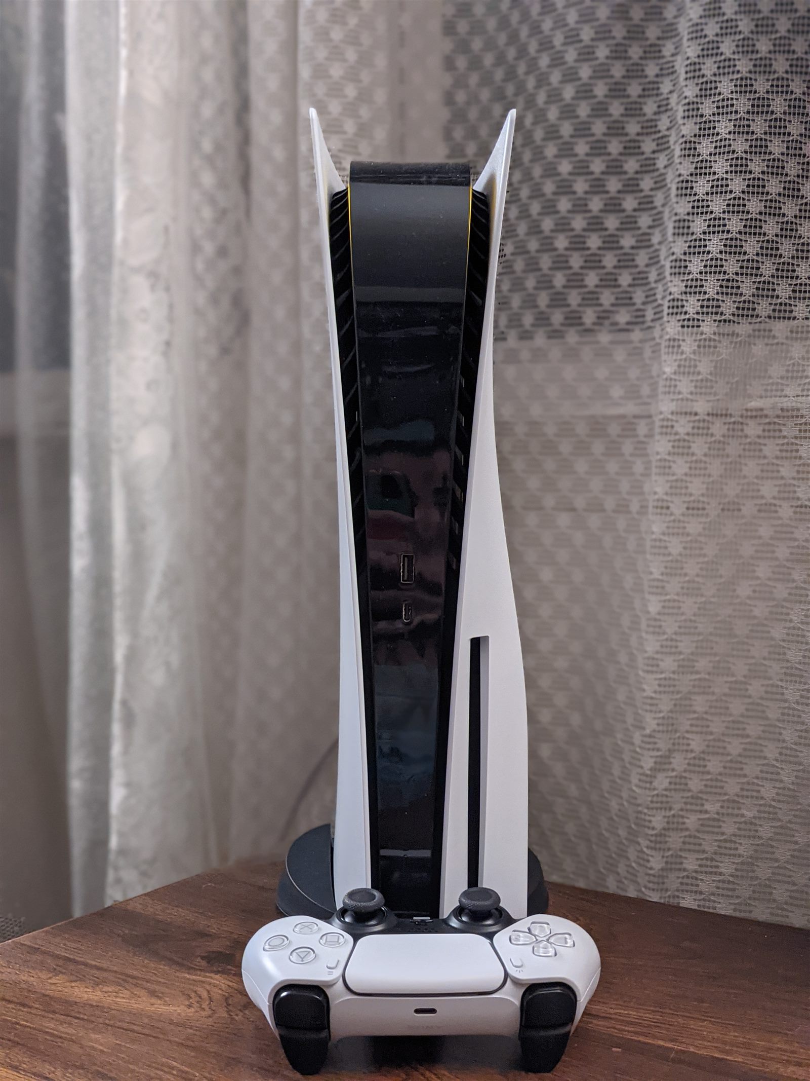 A PlayStation 5 console standing vertically beside its DualSense controller